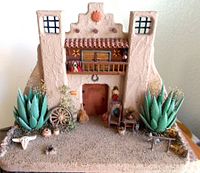 Front view of the Southwest adobe mission model showing detailed miniature plants, pottery, and furniture setup.