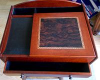 Top view of closed wooden caddy showing a decorative inlaid top panel and velvet-lined tray and slot beside it.