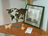 Wide shot showing all four items on wooden shelf: framed photo, metal tree sculpture, stone figurine, and gold leaf flask