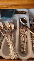 Flatware set organized in drawer utensil tray: forks, spoons, serving utensils with detailed Modern Baroque pattern handles.