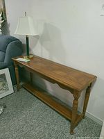Wooden console table with carved patterned top and lower shelf next to a wall, lamp on top.