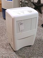 Front and side view of the white Garrison dehumidifier on carpeted floor with visible front vents and top controls.