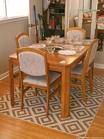 Full view of oak dining table with chairs arranged around it, items including decorative glassware on top (not included).