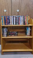 Front view of wooden shelf unit with DVDs and VHS tapes on shelves against wooden closet doors.