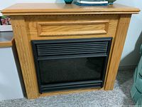 Front view of electric fireplace surround with insert showing oak wood grain and black electric insert with vent slats.
