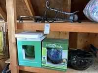 Photo of two boxed gazing balls and black metal plant pot stand on a wooden shelf