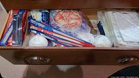 Drawer with various knitting needles in packaging, partial balls of yarn including a multicolor skein, and white yarn balls.