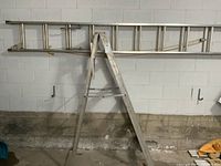 Both ladders visible; step ladder is aluminum with wear marks, extension ladder is mounted on wall, aluminum with locking mechanism