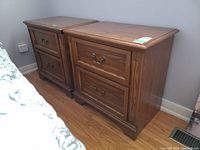 Photo showing the pair of two-drawer wooden night stands side by side against a wall.