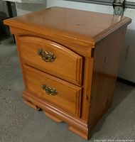Front view of pine night table showing two drawers with brass pulls and carved base molding.