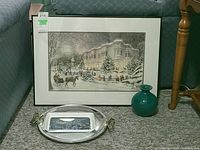 Framed winter scene print with black frame next to a turquoise vase and metal serving tray.