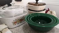 View of three different patterns of Corning casserole pans with lids and three green glass Pyrex Corning mixing bowls on countertop.