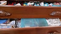 Wooden drawer slightly open showing sewing notions, buttons, embroidery floss, and scissors.