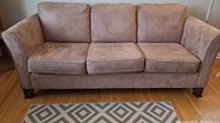 Front view of light brown three-seater sofa with removable seat cushions on wooden floor.