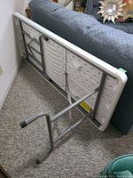 Table folded and leaning against sofa showing underside plastic surface and metal frame with legs partially extended