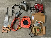 Lot items arranged on floor showing saws, drill, extension cord, and cords