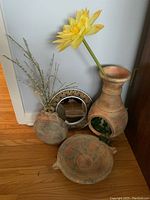 Clay decorative items including a tall vase with yellow flower, mini chimenea, flat bowl, and a round framed mirror with tribal design.