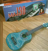 Photo showing Casio MA-130 keyboard box alongside the teal decorative 23-inch ukulele.