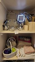 Two shelves showing chrome shower caddies, handheld shower heads, lighted bathroom mirror, toothbrush holder, baskets, hand towels and bath mat.