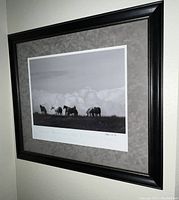 Framed black and white horse-themed poster with visible artist signature on lower right, hung on wall showing matting and black frame.