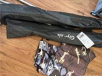 Two black carrying cases with Glymnis branding, one partially open showing camouflage fabric covers, on wooden floor.