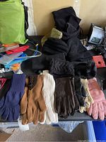 Shows gloves laid out on a table including leather and knitted wool gloves along with winter hats and other winter accessories in background