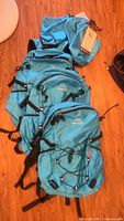 Photo showing three blue HawLander backpacks stacked on floor, each with a blue stuff sack on top