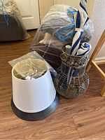 Photo showing decorative metal wire basket holding three folded umbrellas and three fabric throw pillows wrapped in protective covers on floor