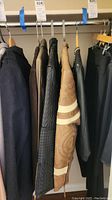 Five jackets hanging on a rack, mostly leather and suede, various styles and colors