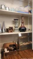 Shelf displaying metal and ceramic vases, a small wooden cuckoo clock, and a wooden planter box filled with rocks and some small decor items.