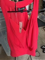 Bright red sleeveless blouse with zipper back, hanging on black hanger; visible price tag attached with NY&C branding.