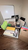 Overall view of multiple office supplies stacked including dry-erase boards, wooden lap desk, clipboards, colored paper, and greeting cards.