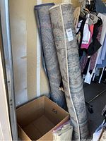 Two rolled outdoor carpets stored upright in garage, bound with cord