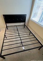 Queen size black steel bed frame with horizontal slats and tufted faux leather headboard placed in a room near a window.