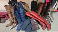 Photo of assorted women's boots including brown leather, blue suede, and red boots in a garage setting