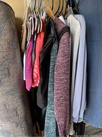 Photo of assorted women's hoodies and casual tops hanging on rack, showing various colors and fabric textures.