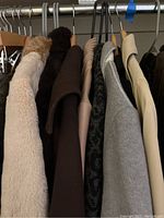Photo of nine women's coats and jackets hung on a clothing rack, various colors and materials shown including faux fur, wool, and knit.