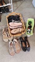 7 pairs of women's sandals arranged on a floor, some in a basket and some outside it, along with several bottles of leather care products in a yellow container.