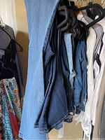 Jeans hanging on black plastic hangers between other clothing; multiple pairs of tall denim jeans in different blue shades.