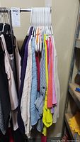 Lot of women's tops including various colors and types of blouses, sweaters, and cardigans hanging on white hangers in a garage setting.