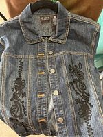 Blue denim jacket with detailed black floral embroidery by Chico's brand.