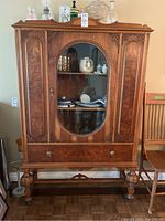 Full front view of the wood china cabinet with glass window in center door, drawer below, and carved legs.