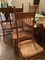 Photo showing a row of four wooden chairs with slatted backs and a carved top rail, highlighting the natural wood grain and finish.
