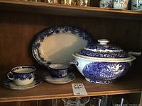 Full view of the blue and white china pieces including soup tureen, oval platter, two tea cups, and saucers.