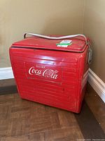 Front view of red vintage Coca-Cola metal cooler with white logo and attached metal handle on top