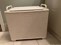 Front angled view of the white painted wicker and wood hamper showing woven wicker pattern and side handle.