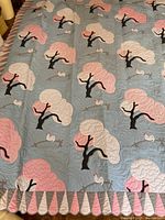 Full view of the quilt showing the blue background with hand appliqued pink and cream trees and white roosters on brown fences, and the scalloped border.