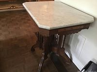 Full side view showing the detailed wood carving on the table base and the attached white marble top with beveled edges.