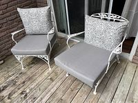 Two white metal patio chairs on wooden deck, showing front and side profiles