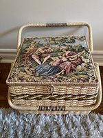 Front view of woven wicker sewing basket with classical tapestry lid and latch closure.